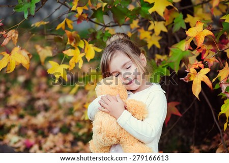 Cute little girl hugging teddy bear toy at autumn background