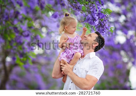 Young beautiful father and his cute daughter love in blooming jacaranda garden