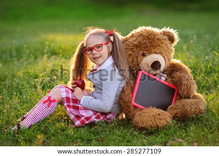 Happy little schoolgirl with chalkboard, health lunch and teddy bear back to school outdoor