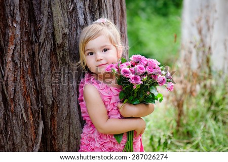 Little toddler lovely girl with flowers in pink dress at beautiful garden