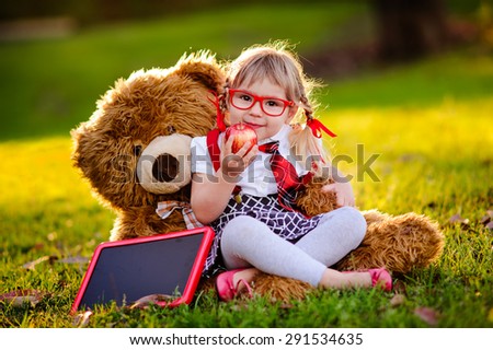 Happy little schoolgirl with chalkboard, health lunch and teddy bear back to school outdoor