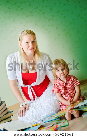 Mother and daughter sit on a floor and read the books and tell fairy tales