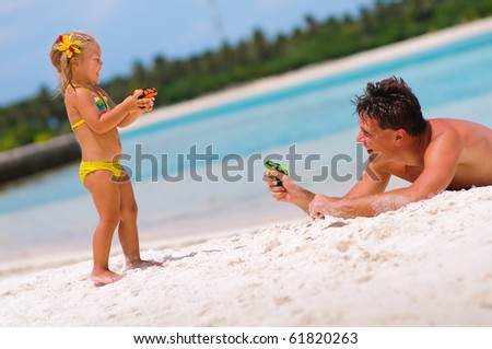 young father and his cute daughter playing with water guns on exotic beach