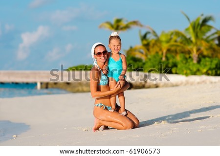 Young mother and her little daughter in bikini on tropical white sand beach in the glow of the evening sun