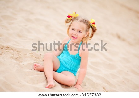 happy little girl in bikini sit on a sand in the beach