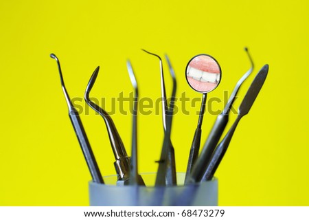 Angled mirror with smile reflection and dental tools in a glass , yellow background