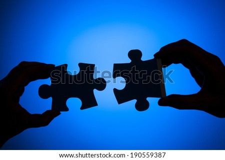 Silhouette of two hands connecting pieces of a puzzle on a blue background