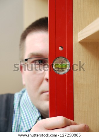 Closeup shot of carpenter looking at spirit level gauge to check verical positioning of furniture - shallow depth of field
