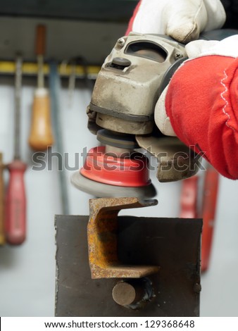 Closeup of machinist worker hands brushing a metal piece using wire brush on angle grinder