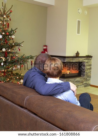Romantic couple sitting on sofa near christmas tree looking at the lit fireplace