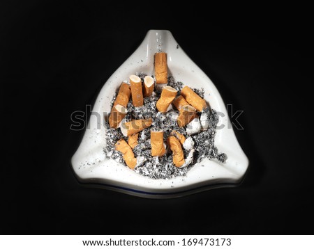 White ceramic ash tray full of cigarette butts on black background