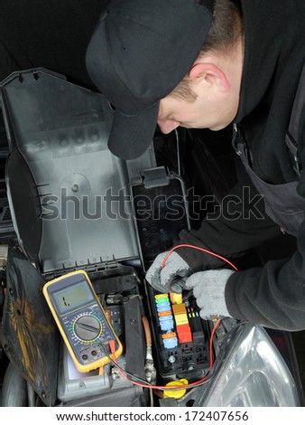 Auto mechanic checking car fuses using multimeter