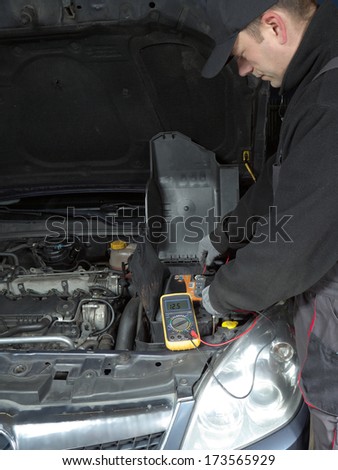 Auto mechanic measuring car battery voltage using multimeter