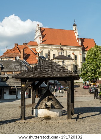 KAZIMIERZ DOLNY, POLAND - MAY 01 2014: Kazimierz Dolny town square with historical wooden well in the center surrounded by picturesque medieval houses and Parish Church Fara on the hill