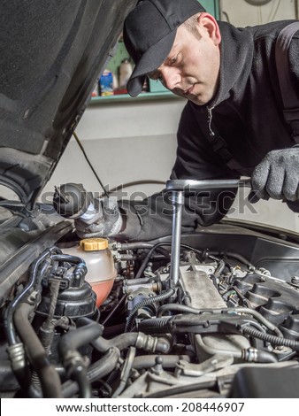 Auto mechanic replacing glow plugs in car diesel engine using spark plug spanner