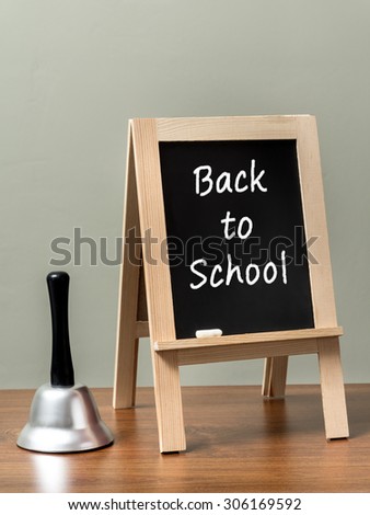 Silver handbell and blackboard with Back to School phrase placed on brown desktop over green wall