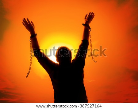 Silhouette of man agains the sunset ssky raising up his hands as he becomes free from chains and shackles