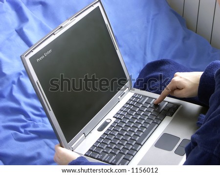 Woman in bed wearing dressing gown with laptop pressing enter key