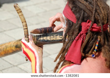 Aborigine-like painted man with dreadlocks playing some primitive wooden instrument