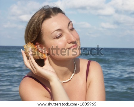 Young woman in bikini at the beach putting sea shell up to her ear and listening its murmur