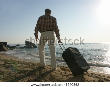 Young man pulling black traveling bag along seaside