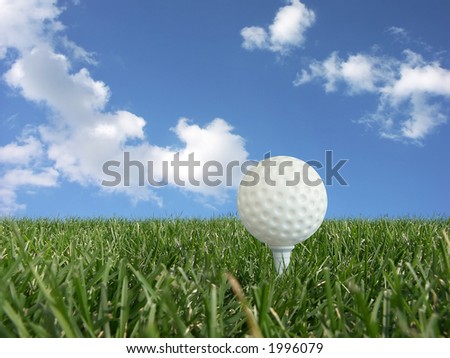White golf ball on a tee in grass over blue sky - low perspective