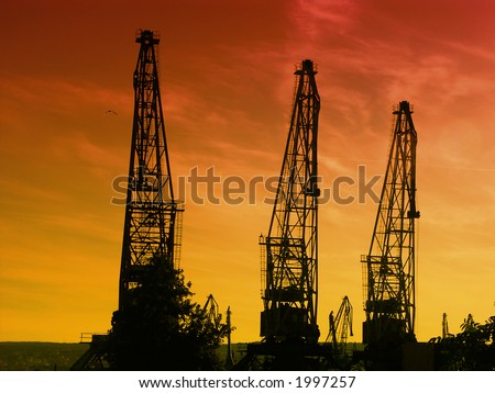 Silhouettes of giant cranes at the port of transhipment against a bloody sunset sky