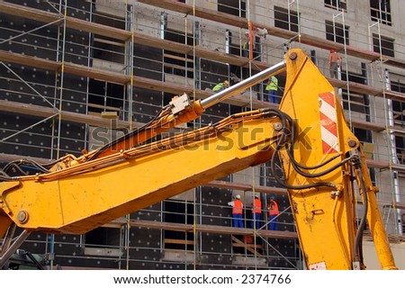 Yellow digger against raw concrete building and construction workers working on scaffolding