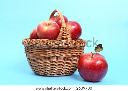 Wicker basket of red apples, one out of basket - over light blue background