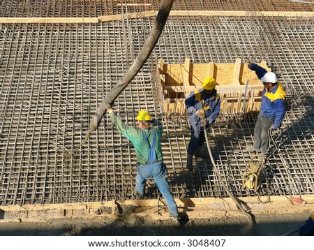 Three construction workers pouring concrete mix into reinforced structure at the building site