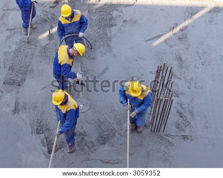 Group of construction workers spreading out fresh concrete mix at the building site