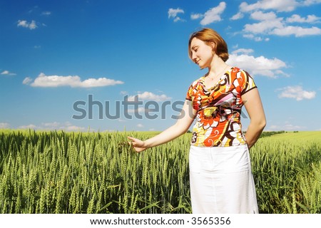 Dreamy girl wearing flowered blouse and white skirt standing in wheat cornfield touching delicately corn ears with her palms