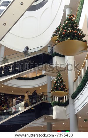 Shoppers using elevator in shopping mall decorated with christmas trees