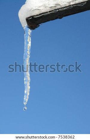 Large icicle formed at the end of roof gutter against clear blue sky