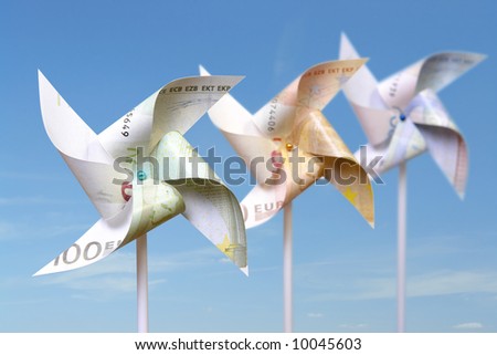Three toy windmills cut from 100, 50 and 20 euro banknotes over blue sky