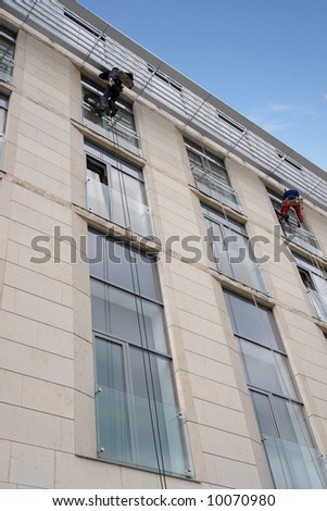 Two window washers washing office building windows hanging outside the building on ropes