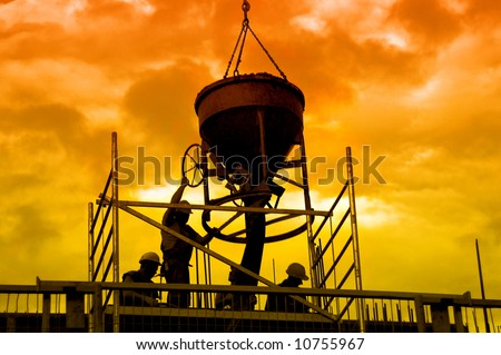 Silhouettes of construction workers pouring concrete mix at the building site over sunset sky