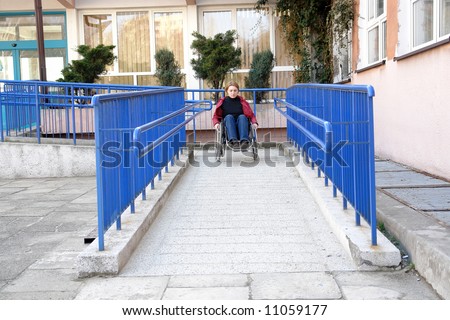 Handicapped woman on wheelchair leaving the building using ramp for disabled