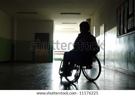 Silhouette of handicapped woman sitting on wheelchair in hospital hallway looking towards the light coming throuth the window