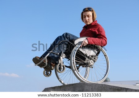 Wheelchair woman balancing by the concrete kerb over blue sky