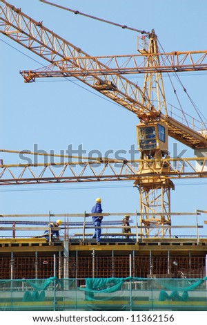 Construction workers working at building elevation with jib cranes in the background