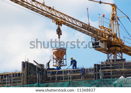 Construction workers pouring concrete mix from charging hopper transported by jib crane