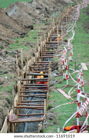 Construction workers working in long earth excavation protected on two sides by wooden shuttering