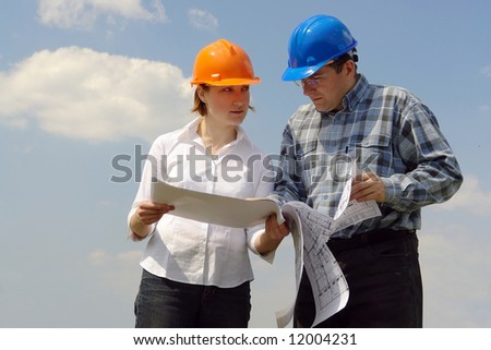 Female investor and site manager discussing building plans over blue sky