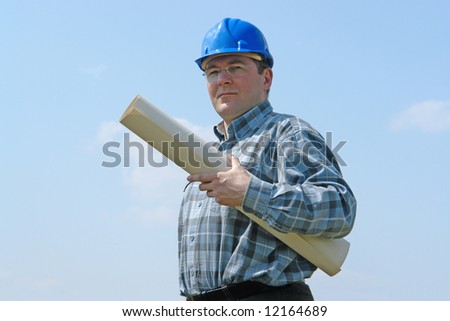 Construction site manager wearing blue helmet holding roll of building plans over blue sky
