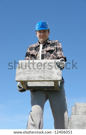 Construction worker in blue hard hat carrying concrete shuttering block