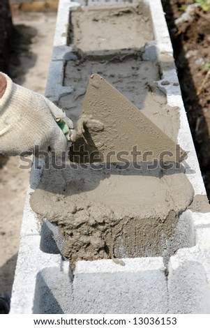 Closeup of mason hand spreading mortar with trowel in concrete shuttering blocks as house foundation