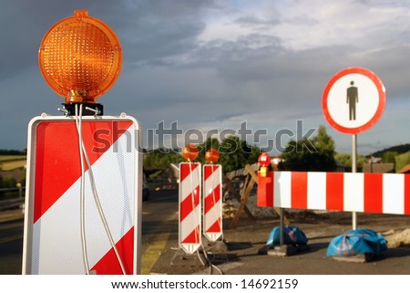Road works marked with red and white striped road warning posts with orange beacons and barrier with no access sign