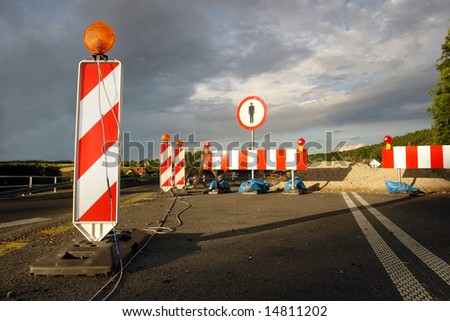 Road works marked with red and white striped road warning posts with orange beacons and barrier with no access sign