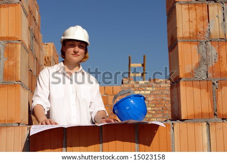 Female investor wearing white helmet standing inside unfinished house window opening studying building plans